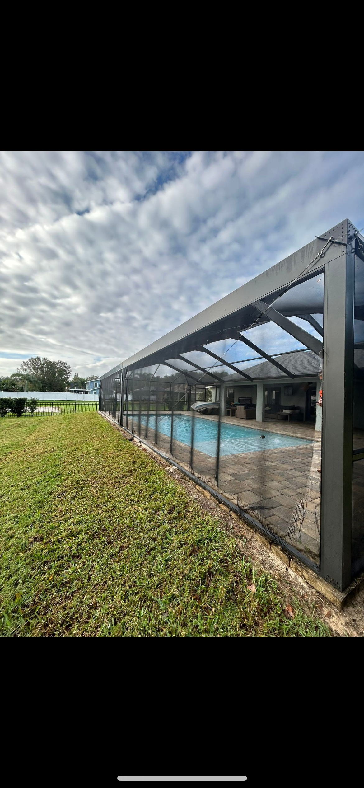 A screened-in pool area with a covered roof, surrounded by green grass and a cloudy sky.