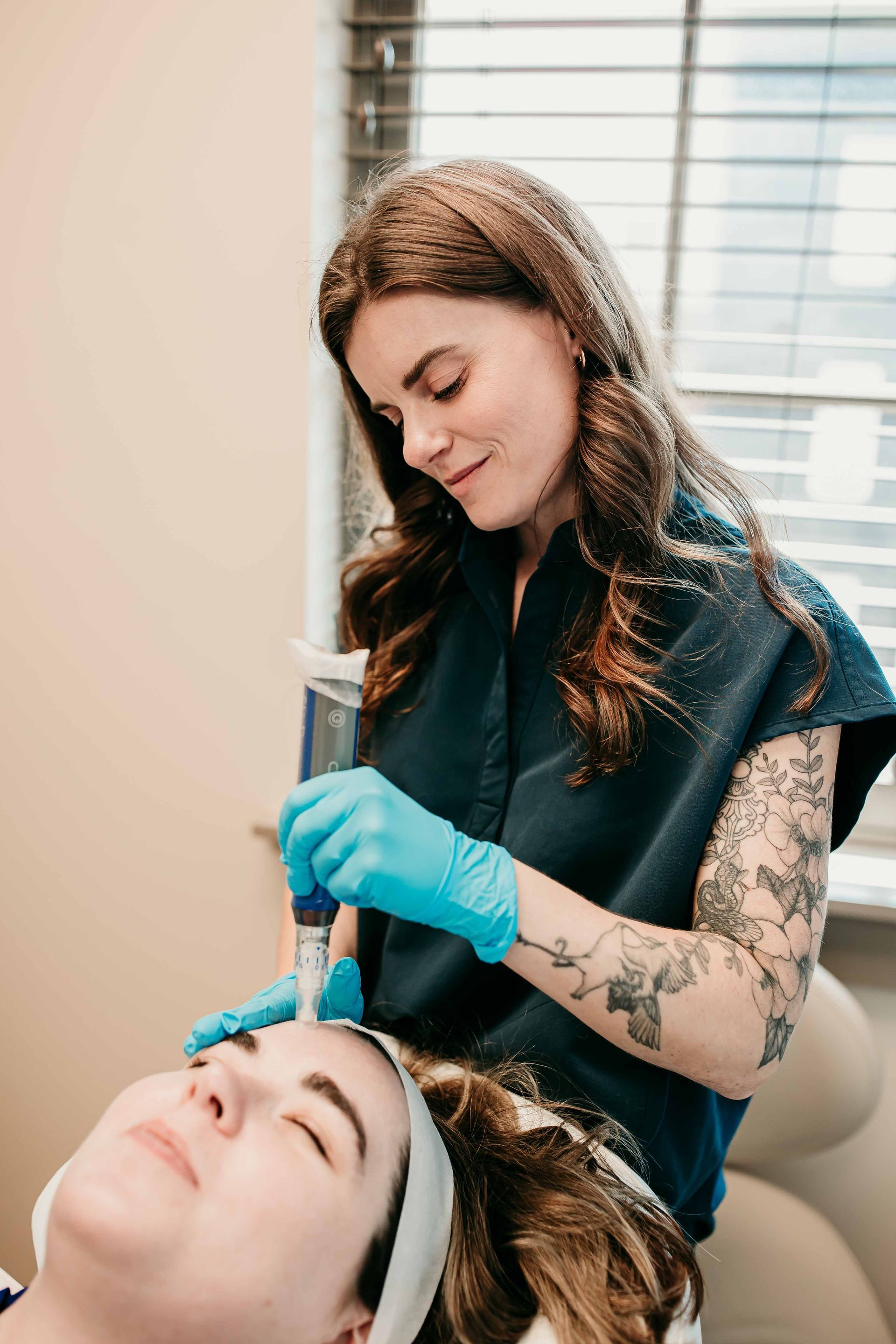 Cosmetologist in blue gloves applying treatment to a client’s forehead in a spa room