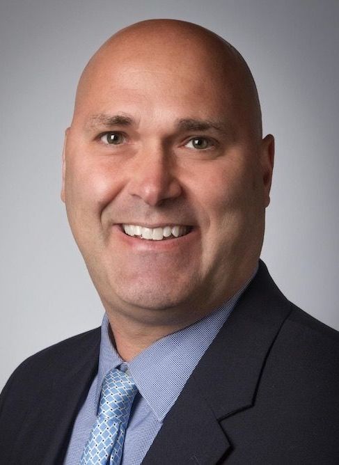 A bald man in a suit and tie is smiling for the camera