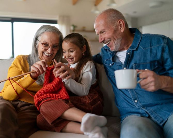 A family is sitting on a couch knitting together.