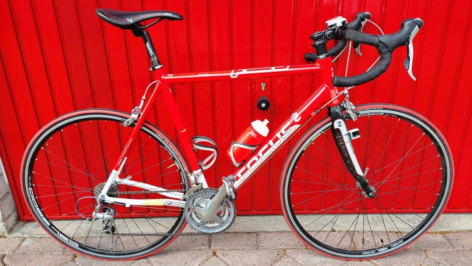 Rode racefiets met witte letters tegen een rode garagedeur.