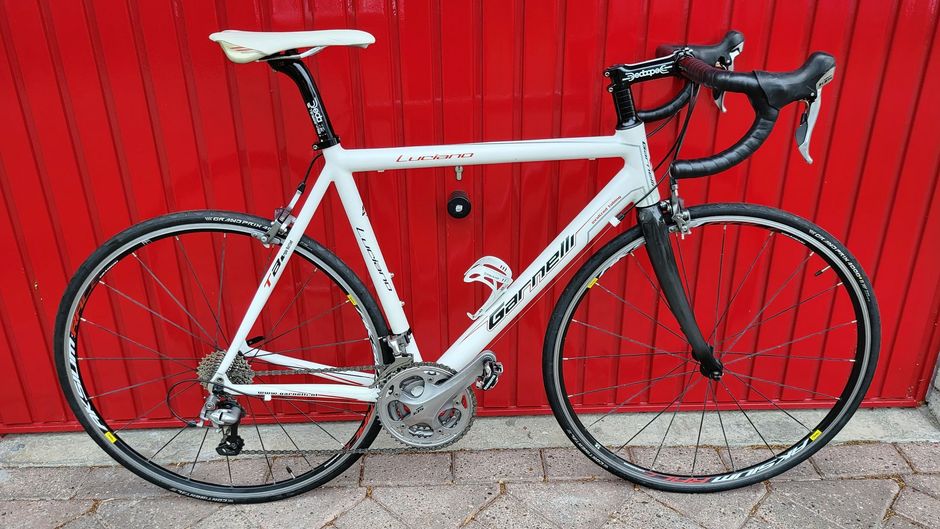 Witte racefiets met zwarte voorvork tegen een rode achtergrond.