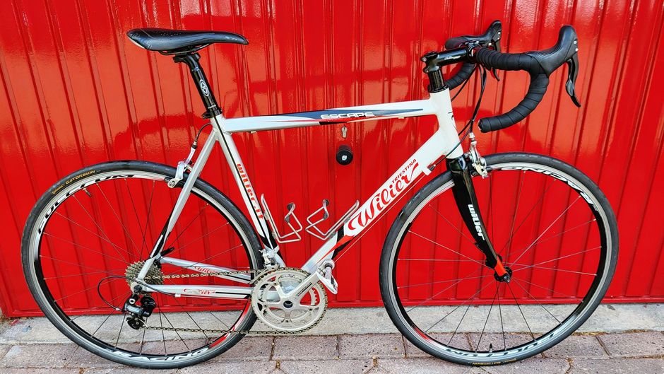Een witte en rode Wilier racefiets staat tegen een rode deur.