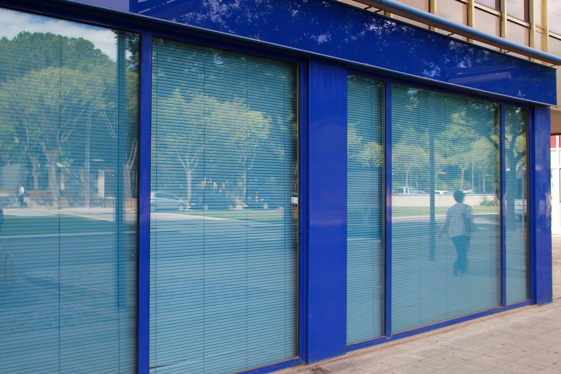 Blue storefront with reflective glass windows and a closed door along a sidewalk