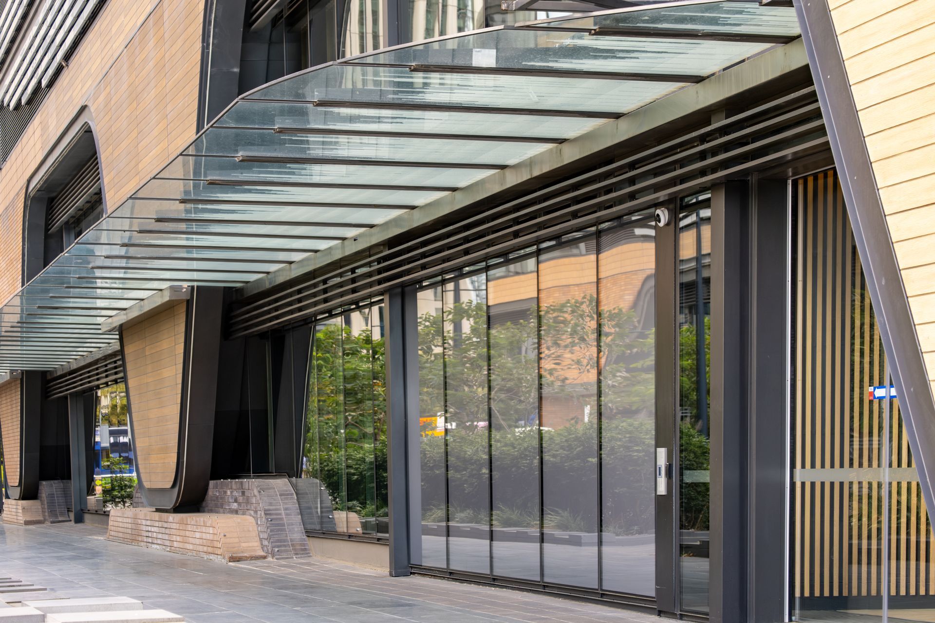 Modern storefront with glass doors, black columns, and a glass canopy along a sidewalk