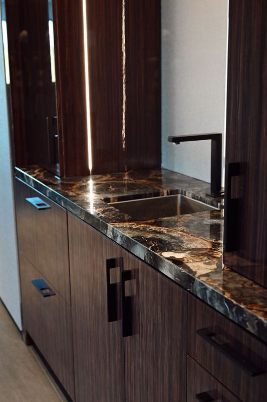 Modern kitchen sink with dark wood cabinets and marble countertop by a window