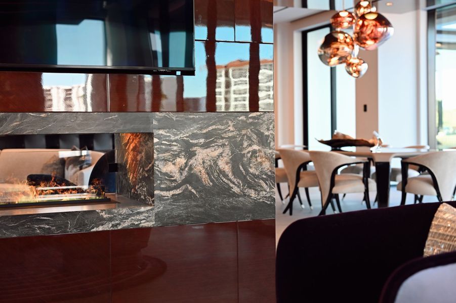 Modern lounge with marble fireplace, wood floors, and a dining table by large windows