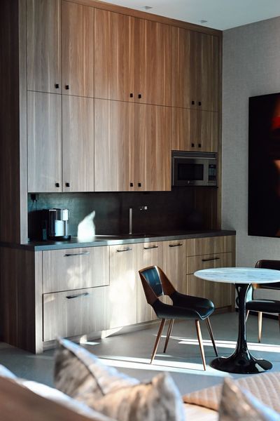 Modern kitchenette with wood cabinets, dark backsplash, small table, and chairs in a bright room