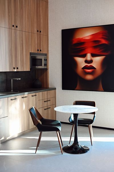 Modern kitchen with two chairs, a small round table, and a large abstract portrait on the wall.