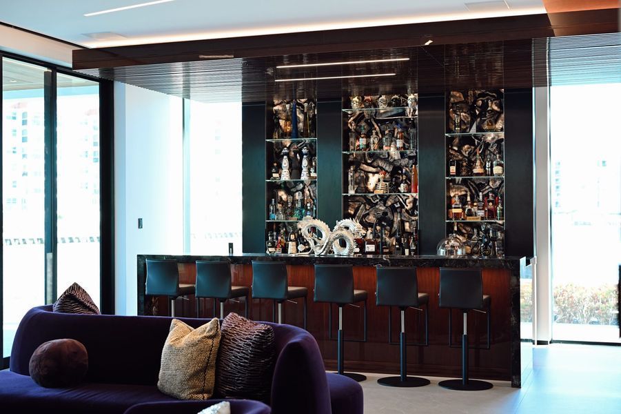 Modern lounge with purple sofa, bar seating, and a glass display wall in a bright room