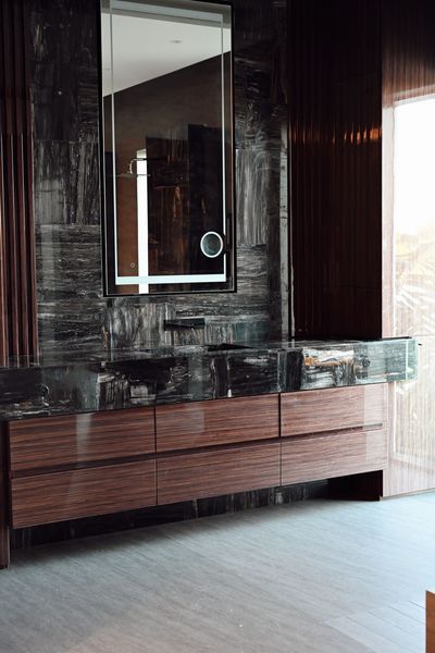 Modern interior with a dark wood dresser, mirror, and glossy black wall panels near a bright window.