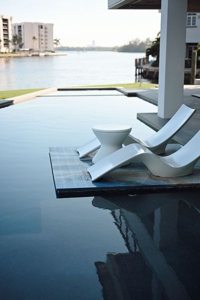 Infinity pool beside modern lounge chairs overlooking a waterfront skyline