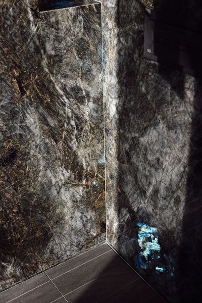 Dark marble walls meeting at a corner with a blue-lit object near the floor
