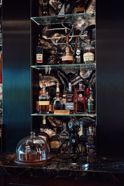 Glass cabinet with liquor bottles and glassware on dark shelves, lit by warm ambient light