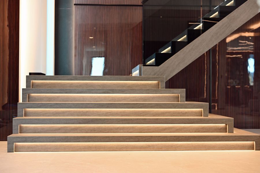 Modern indoor staircase with gray steps and wood-paneled walls, lit by warm ambient lighting