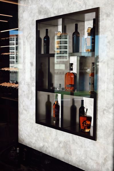 Wall-mounted glass-front liquor cabinet with assorted wine and whiskey bottles on a textured wall