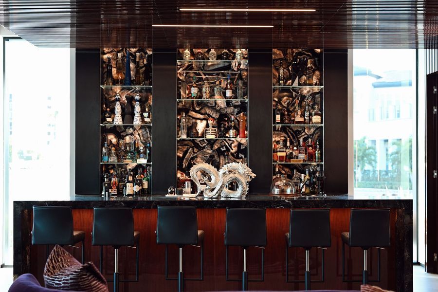 Modern bar interior with mirrored back wall, dark wooden counter, and black stools under warm lighting
