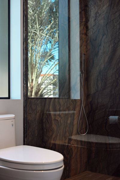 Modern bathroom with a toilet, dark stone wall, and narrow window showing trees outside