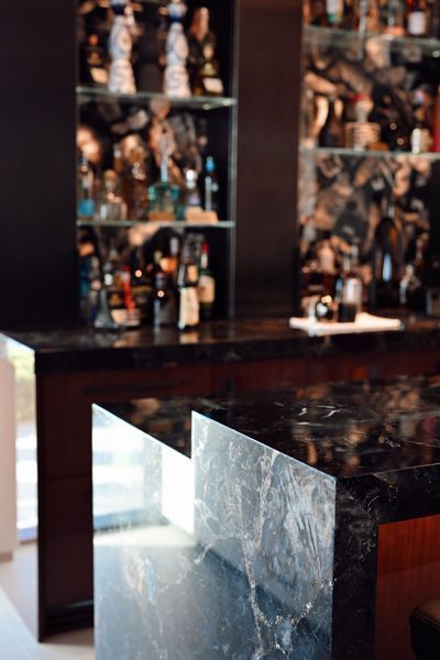 Marble-topped bar with wooden shelves displaying numerous bottles and figurines