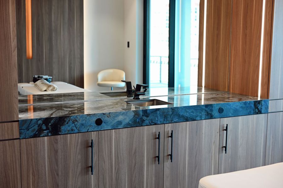 Modern kitchen island with blue countertop, sink, cabinets, and a white chair by tall windows