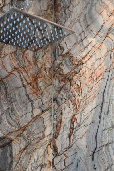 Close-up of a gray and rust-veined marble surface with a metal shower squeegee in the corner
