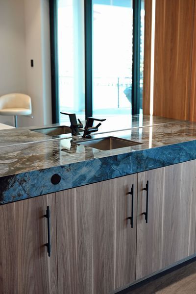 Modern kitchen island with wood cabinets, blue stone countertop, and sink near a bright window and sliding door