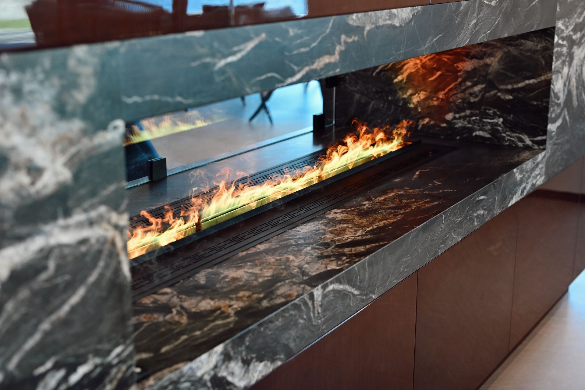 Modern linear fireplace with flames set in a dark marble wall panel