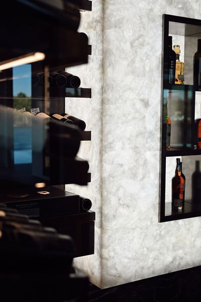 Wine bottles displayed on black shelves beside a white wall in a dimly lit interior.