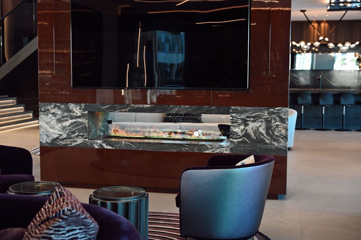 Modern hotel lounge with marble fireplace, large wall TV, and dark leather seating