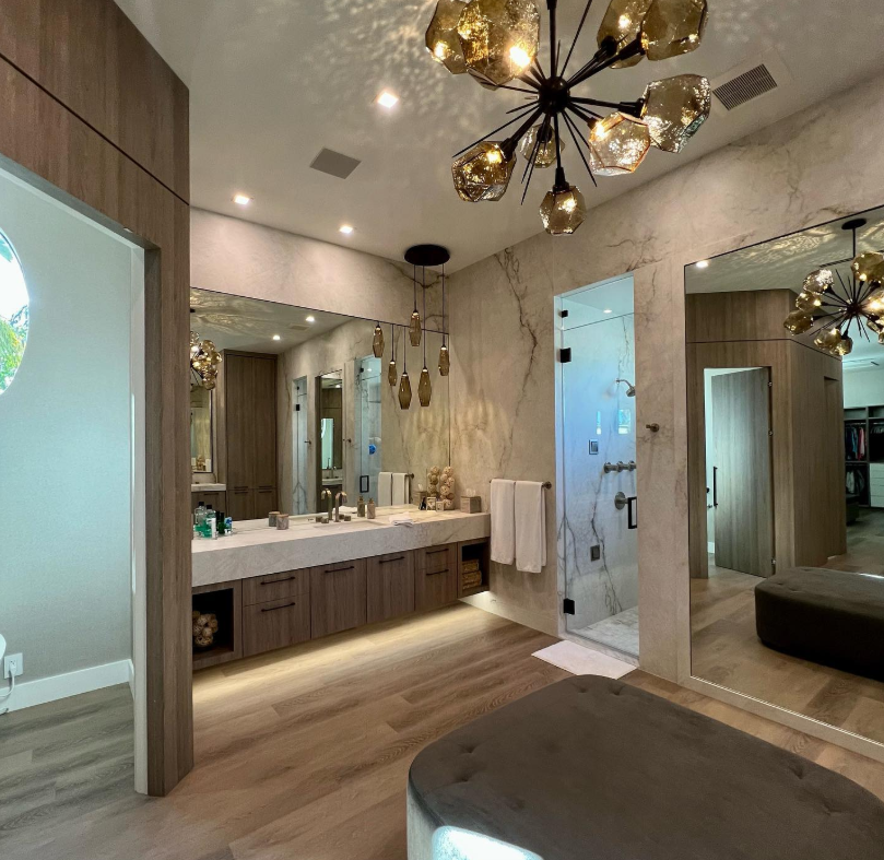 Luxurious bathroom with dual sinks, glass shower, chandelier, large mirror, and light wood flooring