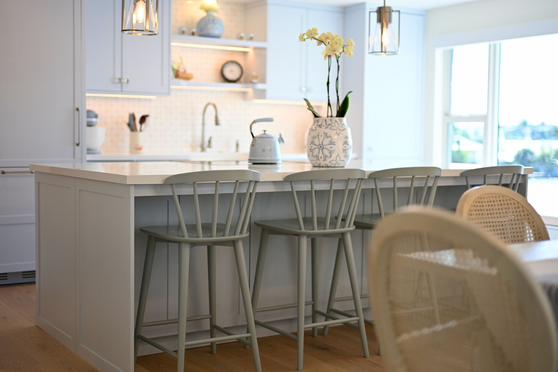 Bright kitchen with a white island, bar stools, and a vase of flowers by a sunny window