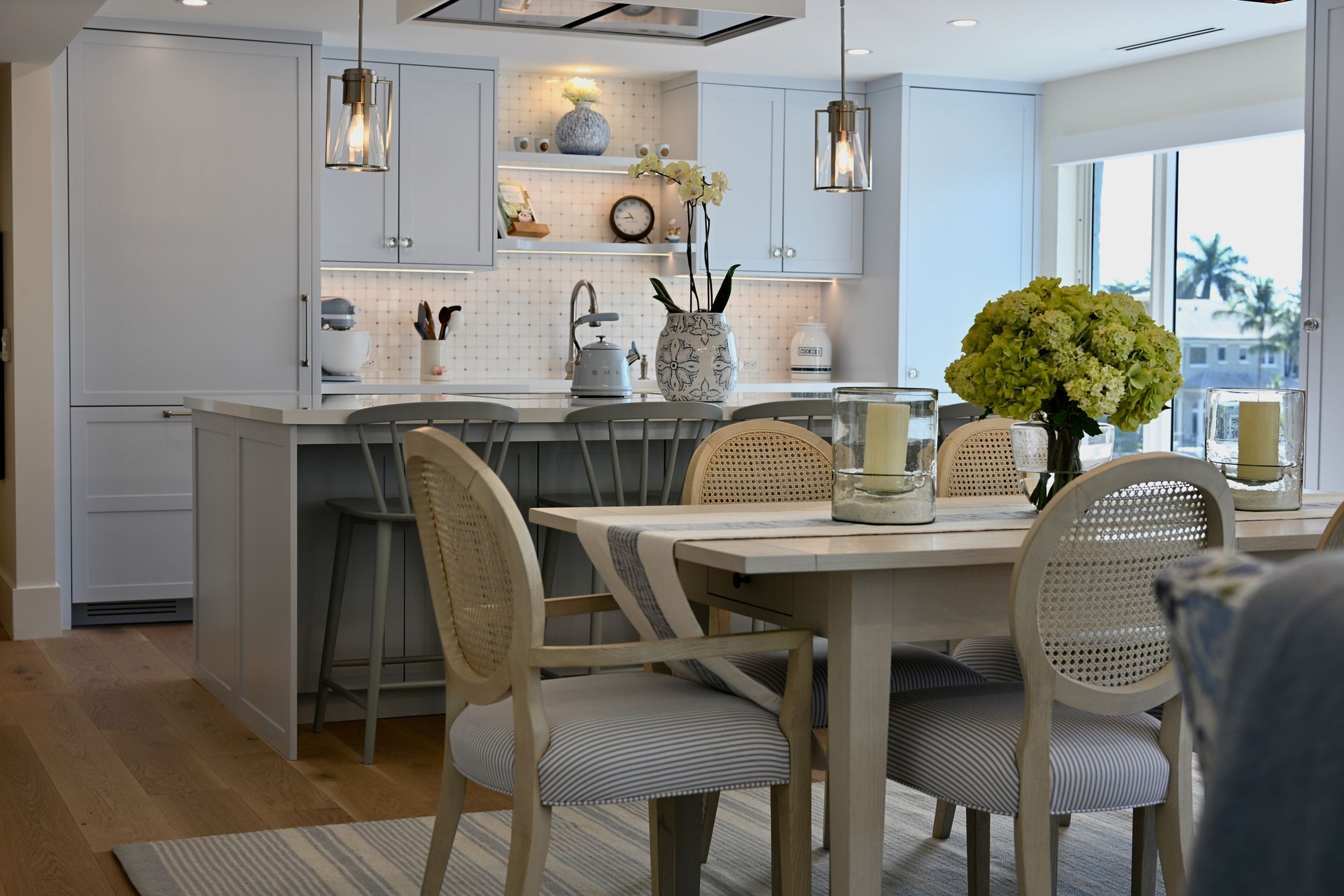 Bright modern kitchen and dining area with white cabinetry, wicker chairs, and a vase of yellow flow
