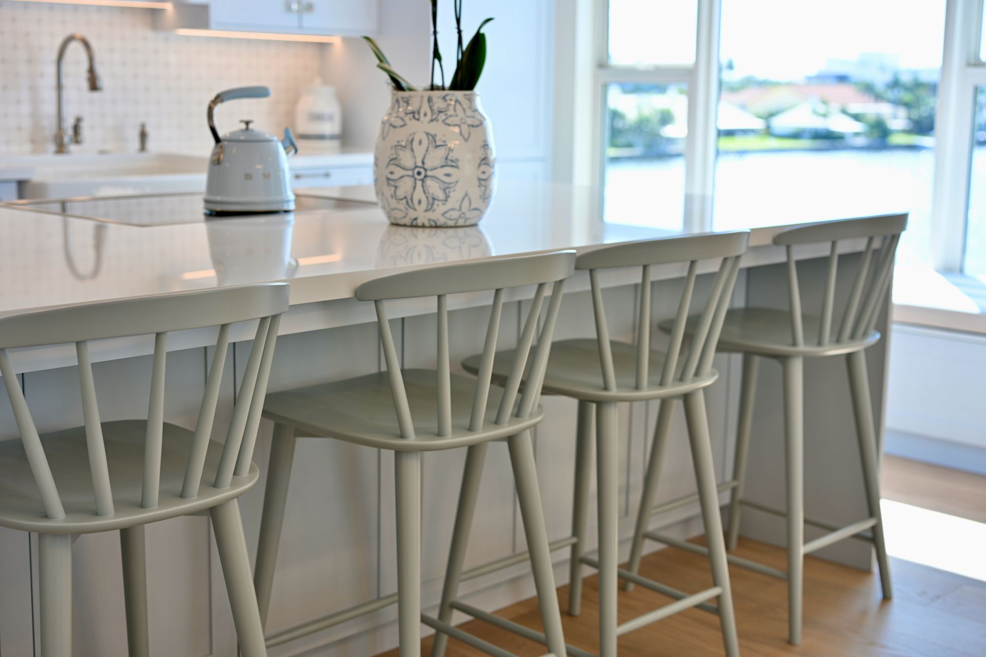 Bright kitchen with a white island, five bar stools, and a large window overlooking water.