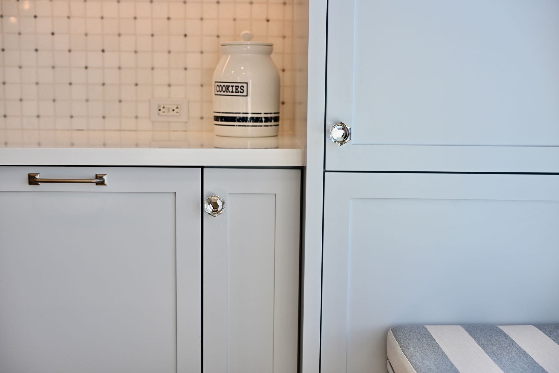 White built-in cabinets with a jar on the counter beside a bed corner in a bright room.