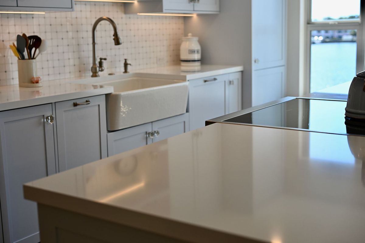 Bright modern kitchen with white island, farmhouse sink, gray cabinets, and a sunlit window