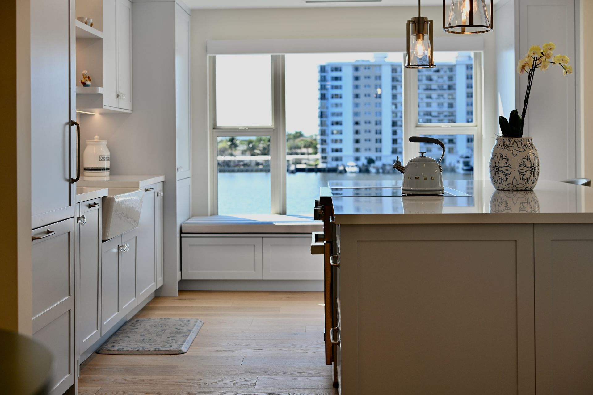 Bright modern kitchen with white cabinets, island, and large windows overlooking the water and city buildings