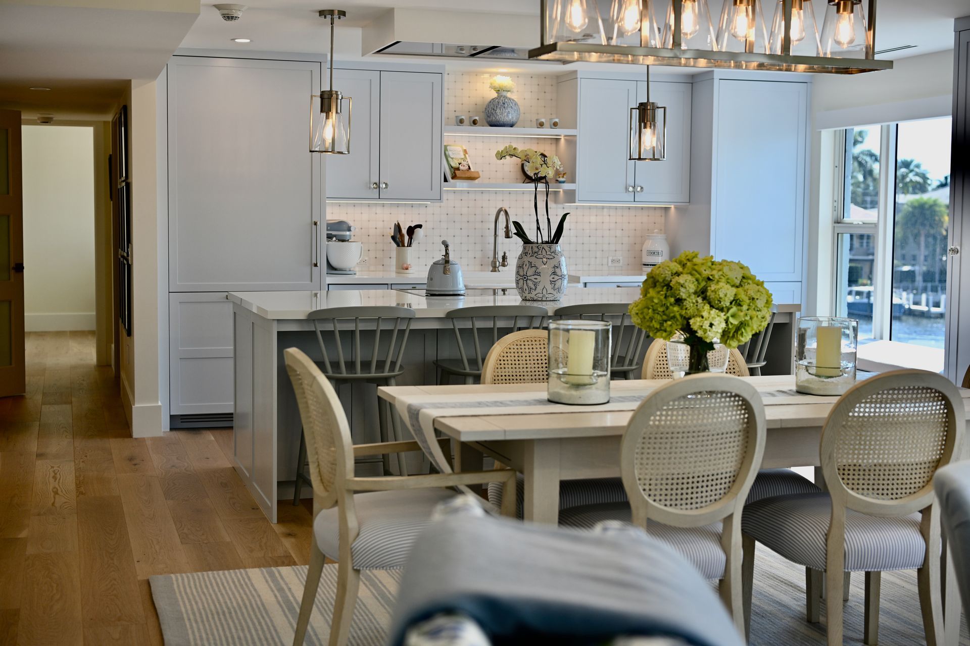 Bright dining area and white kitchen with wood floors, island seating, and a vase of green flowers at the table