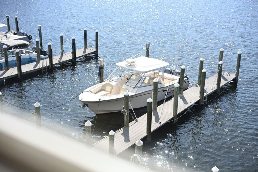 White motorboat docked at a wooden pier on blue water, with empty slips nearby.