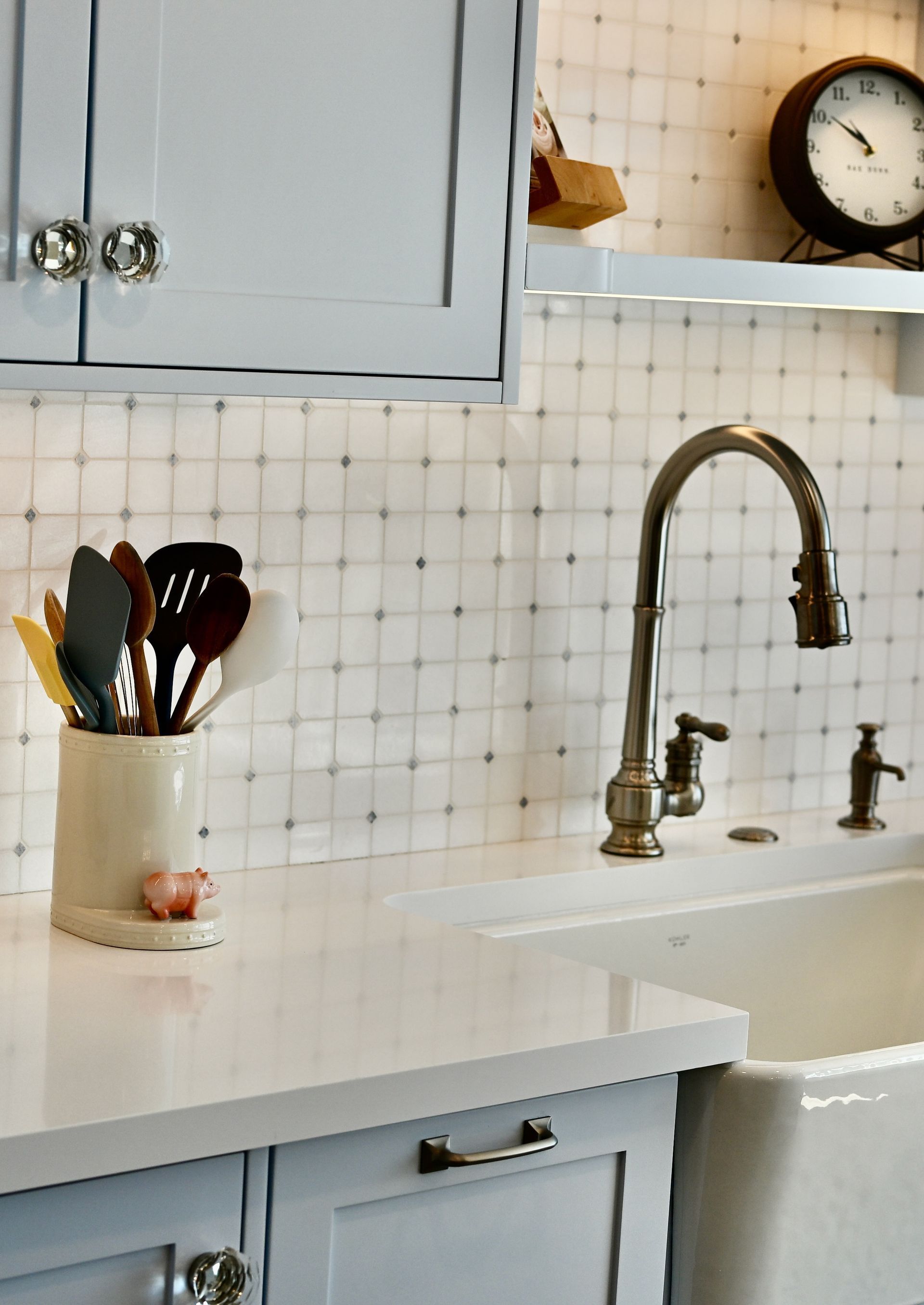 Bright kitchen sink with blue cabinets, white tile backsplash, and utensils in a countertop jar