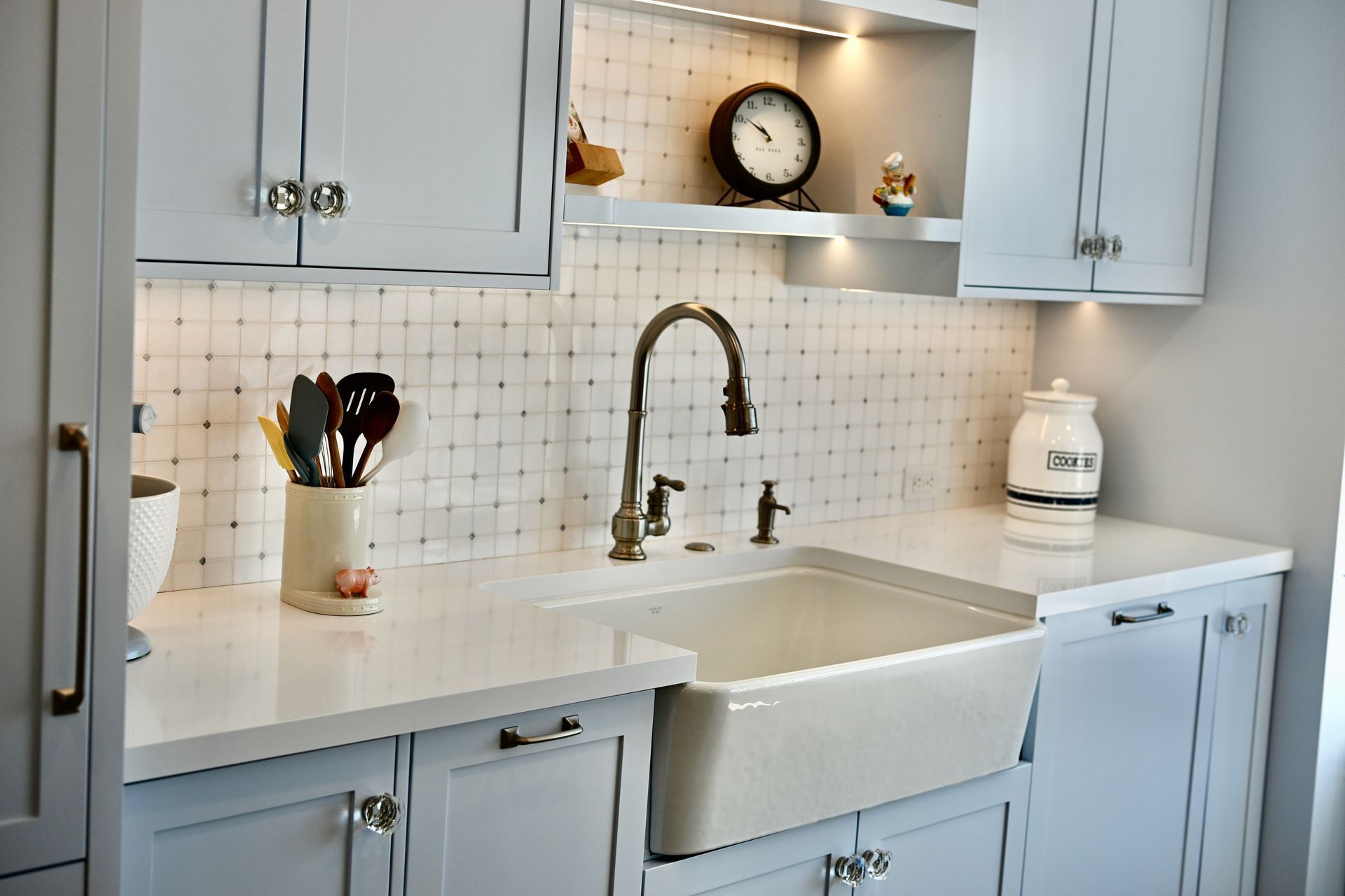 Light blue kitchen sink area with white cabinets, tiled backsplash, and countertop decor
