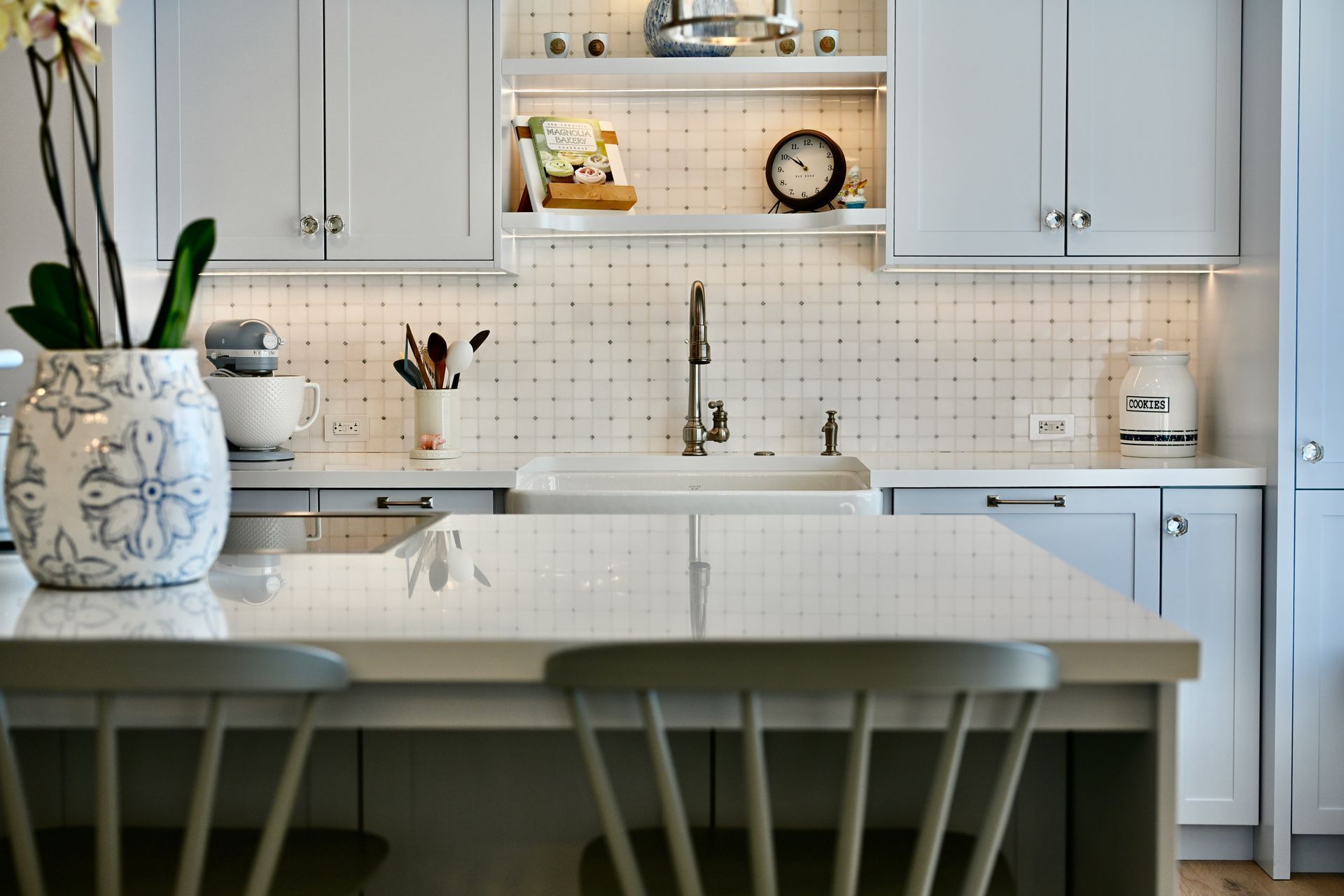 Bright white kitchen with marble island, pale cabinets, subway tile backsplash, and potted plant on the counter