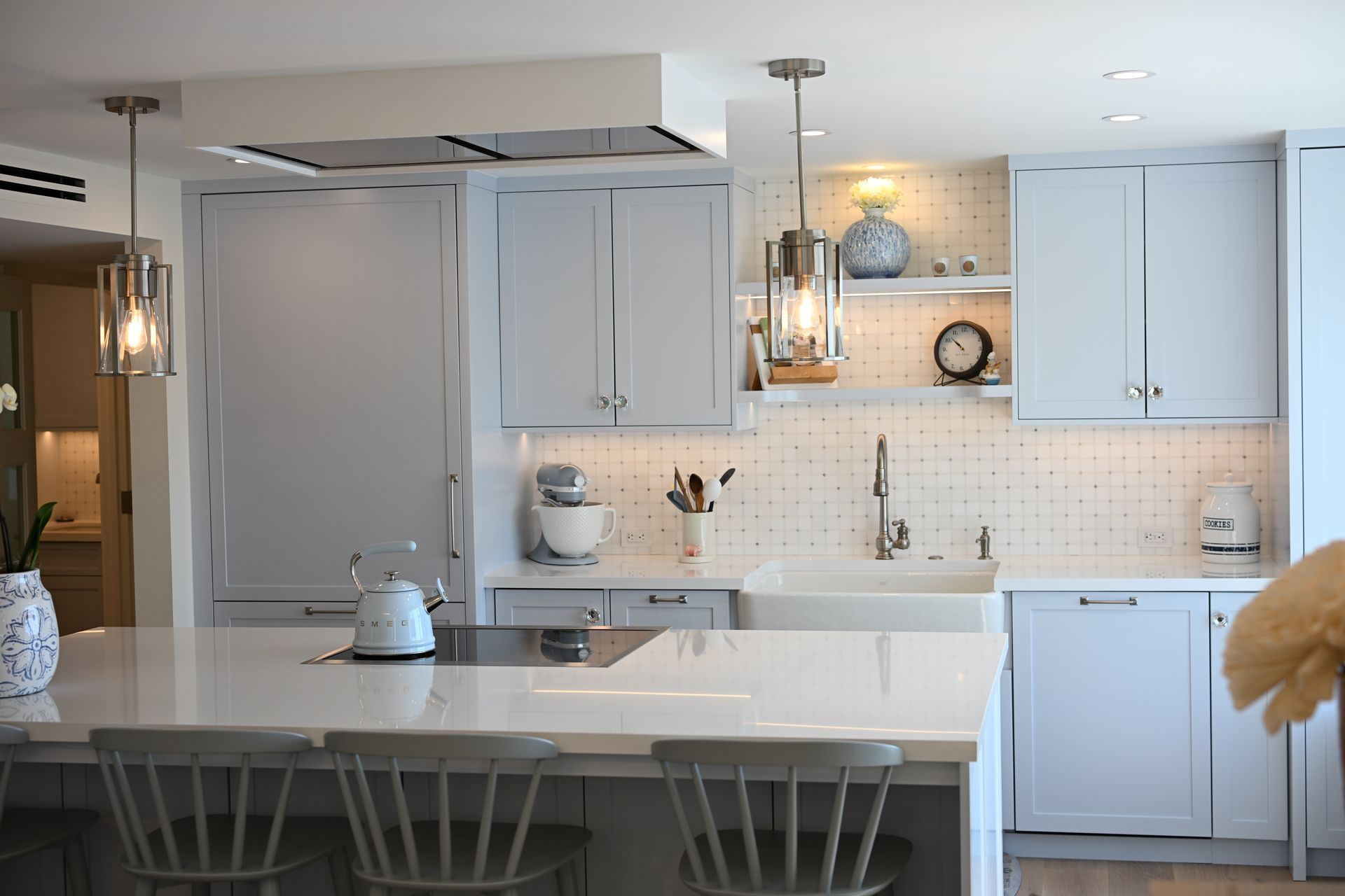 Bright white kitchen with island, pendant lights, cabinets, and a teapot on the counter