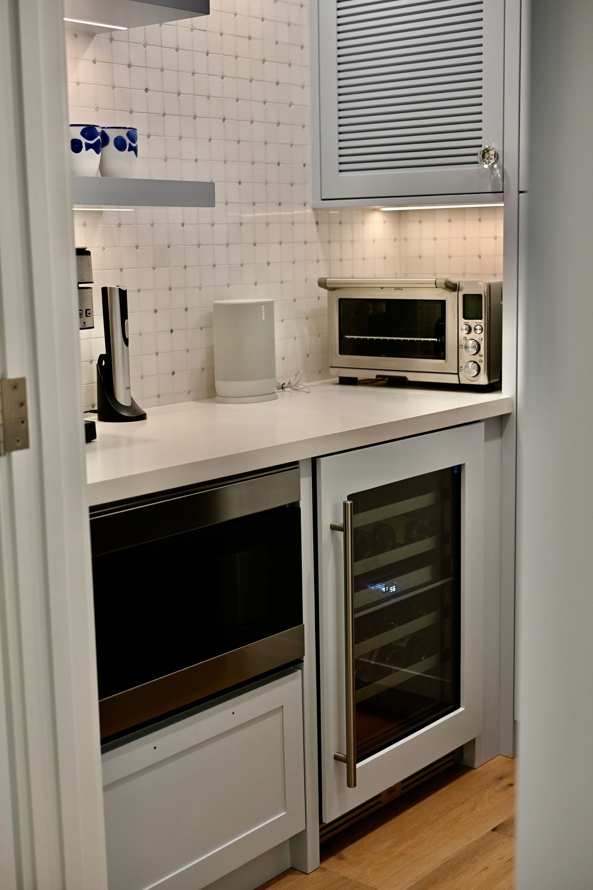 Compact white kitchen with microwave, oven, and black countertop appliances under a window blind