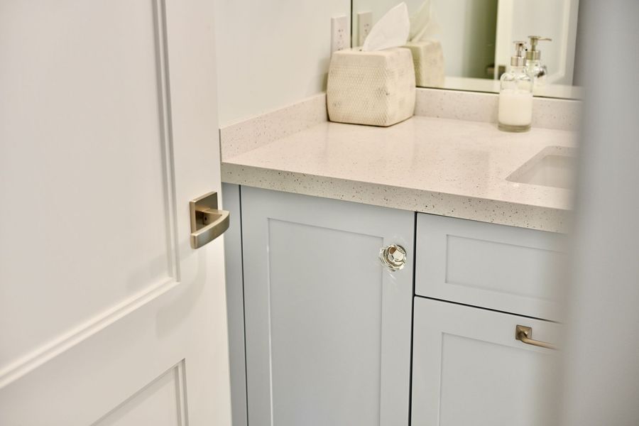 Bathroom vanity with light gray cabinets, white countertop, and tissue box near a mirror