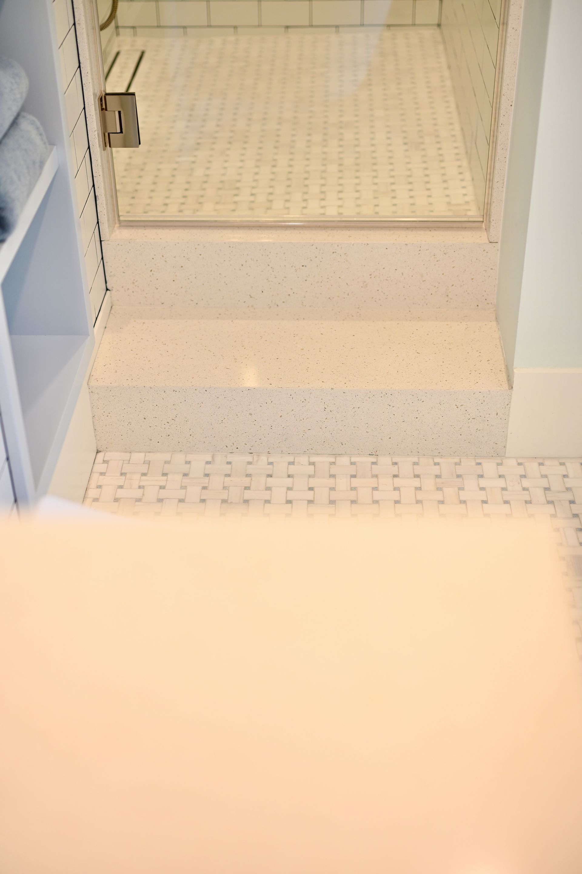 White tiled shower stall with a built-in shelf and step-up ledge, viewed from the bathroom floor.