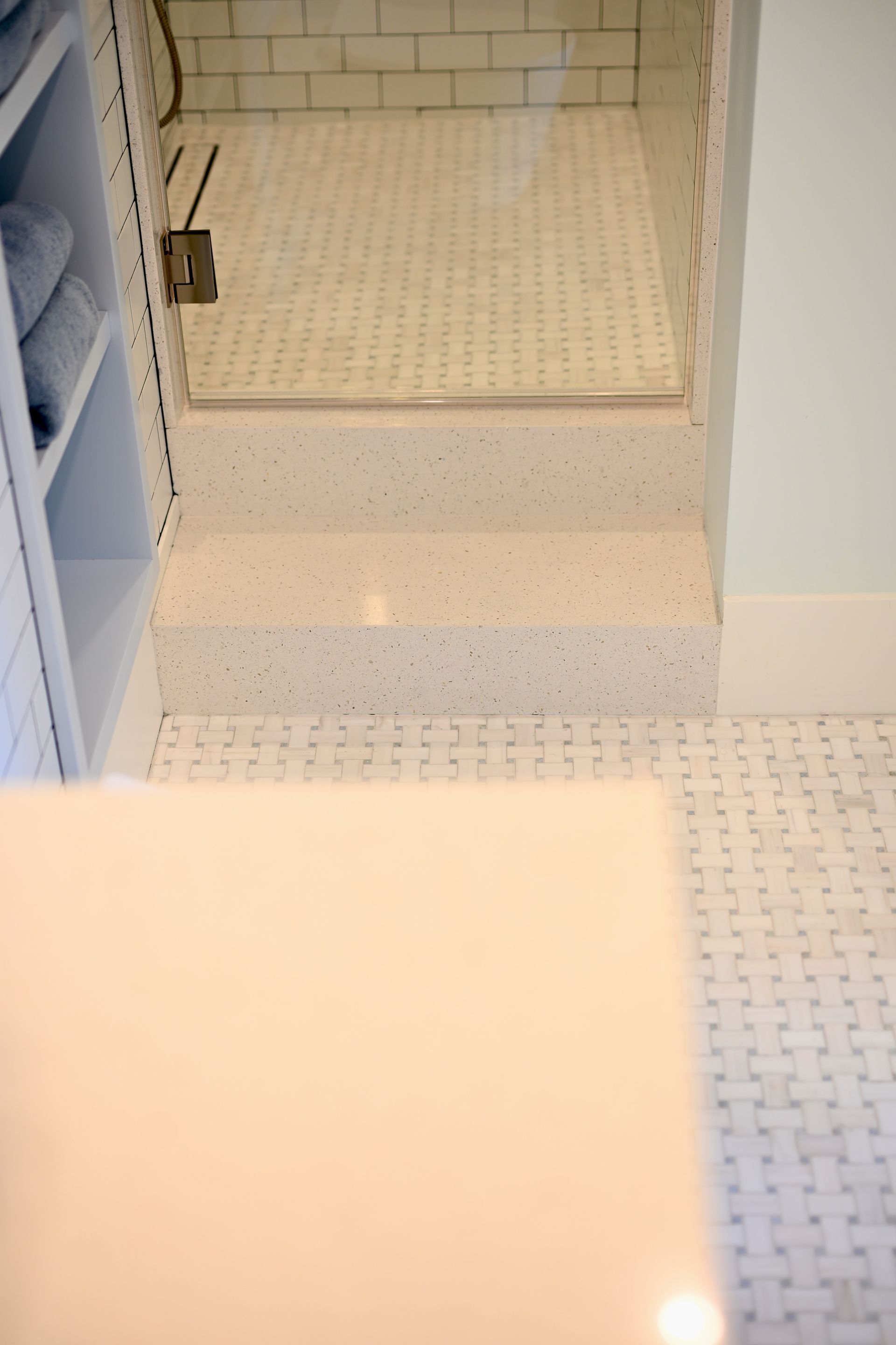 White tiled bathroom with a step up to a shower or tub area and a visible shower drain.