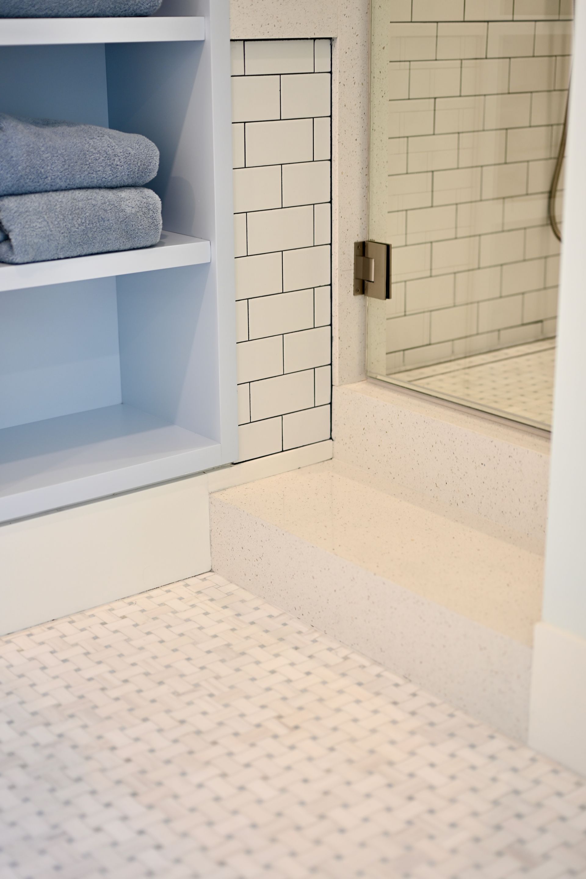 White bathroom with built-in shelves, towels, shower, and a small step-up into the shower area.