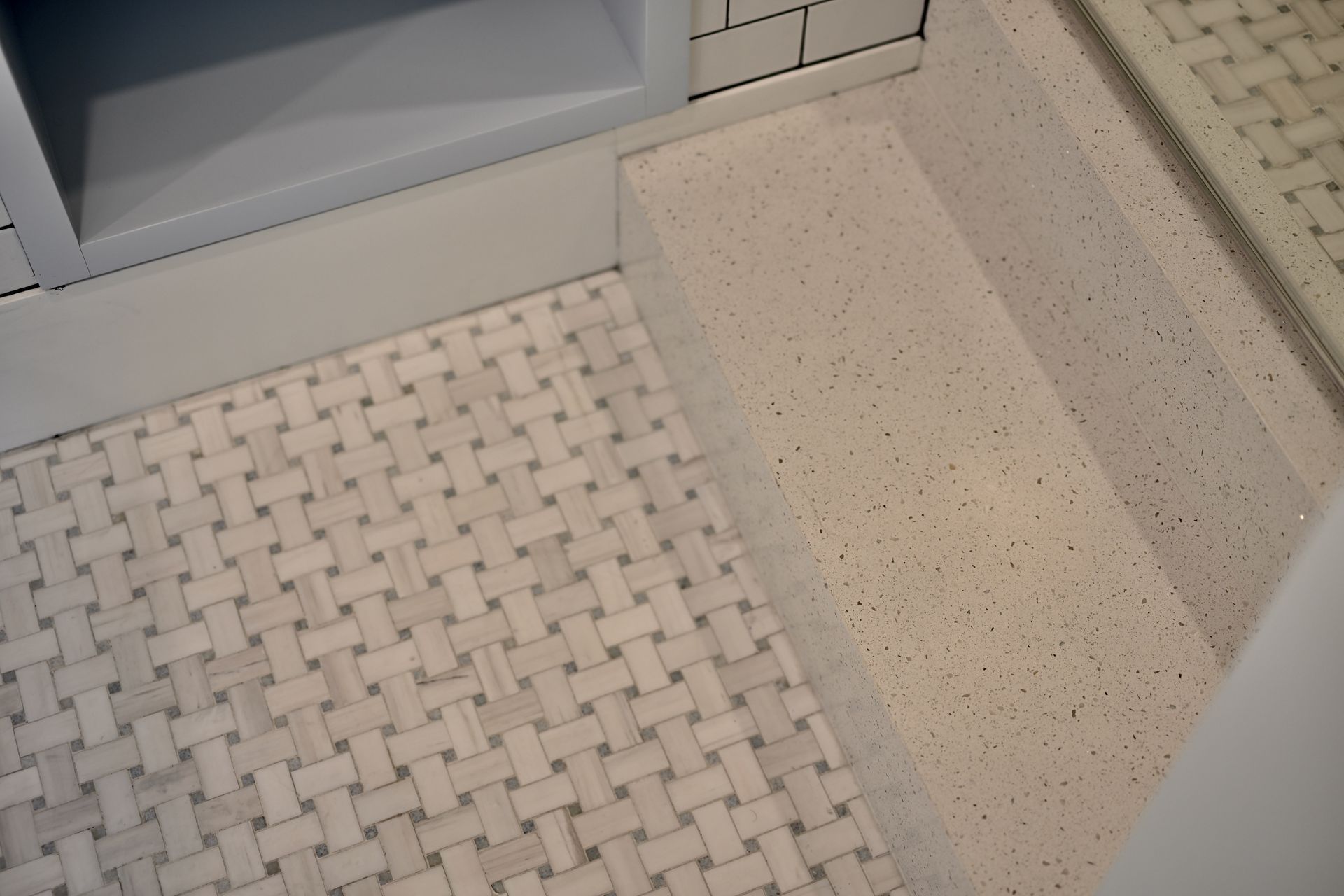White mosaic tile floor beside a speckled stone step and cabinet base in a bathroom or kitchen area