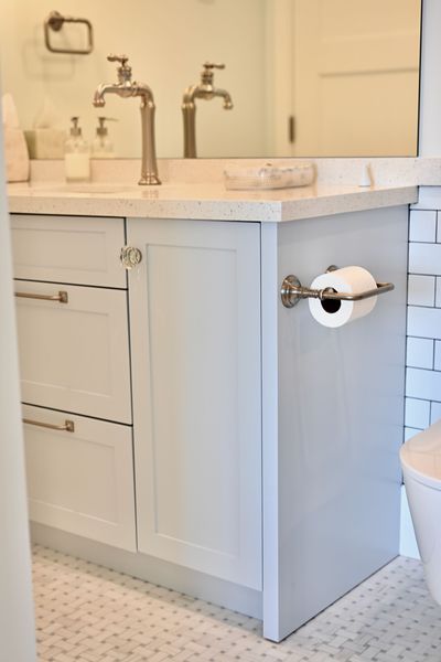Bathroom vanity with white countertop, double faucets, and toilet paper holder on the side.