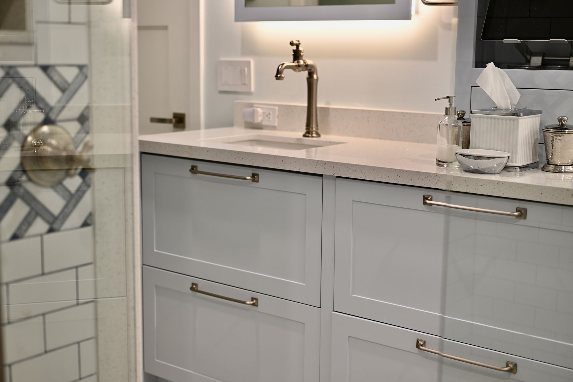 Bright bathroom vanity with white cabinets, marble countertop, gold faucet, and decorative tile wall.